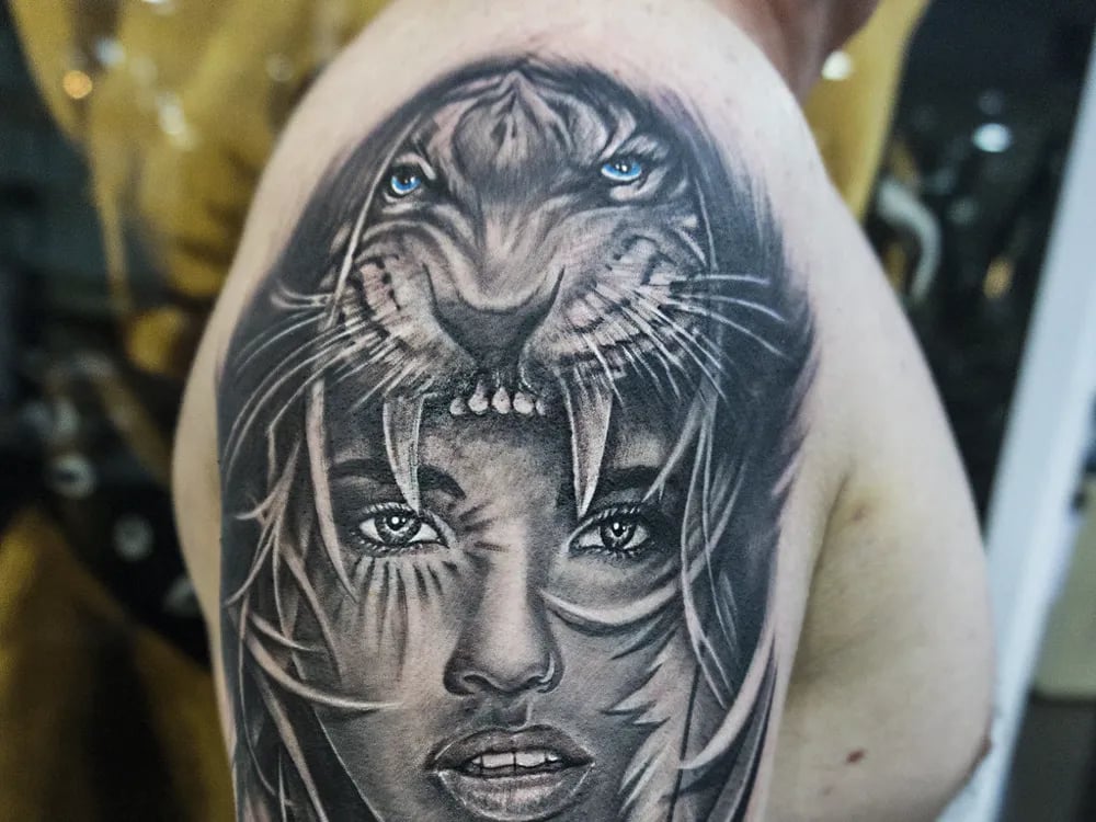 Black and grey portrait of a woman beneath a tiger on an upper arm