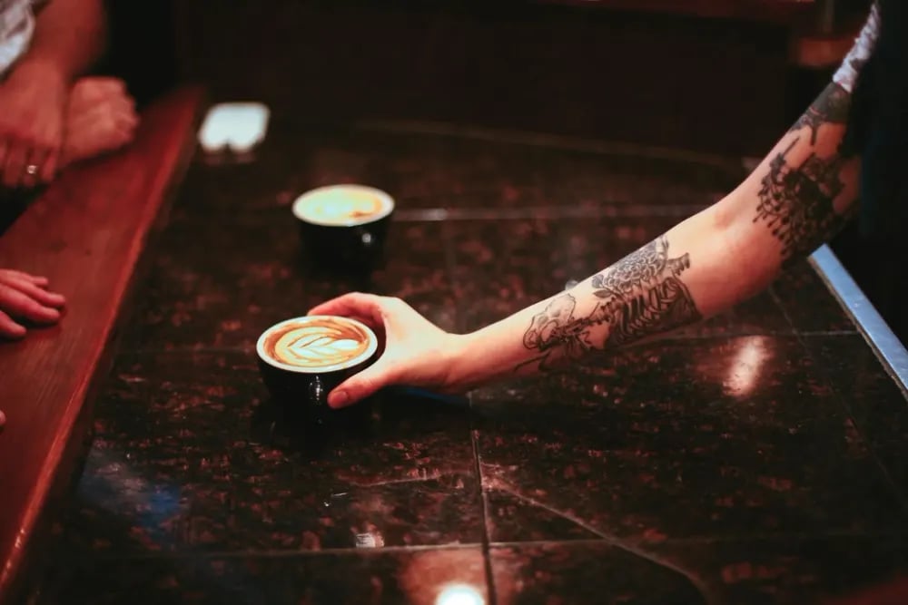 Forearm with detailed blackwork tattoo reaching for a coffee cup