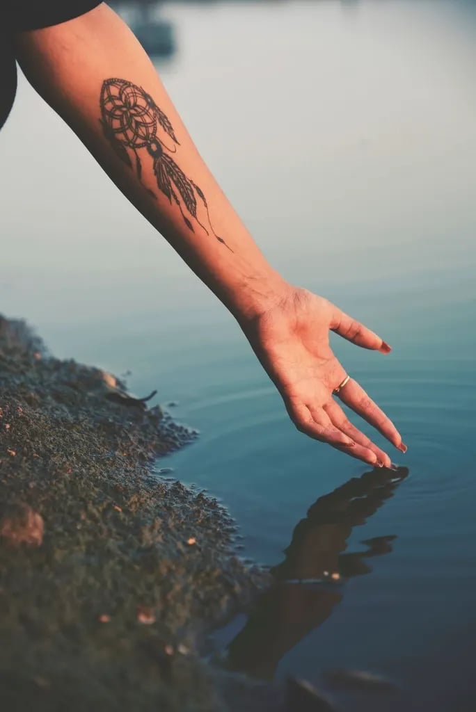 Dotwork dreamcatcher on a forearm above water